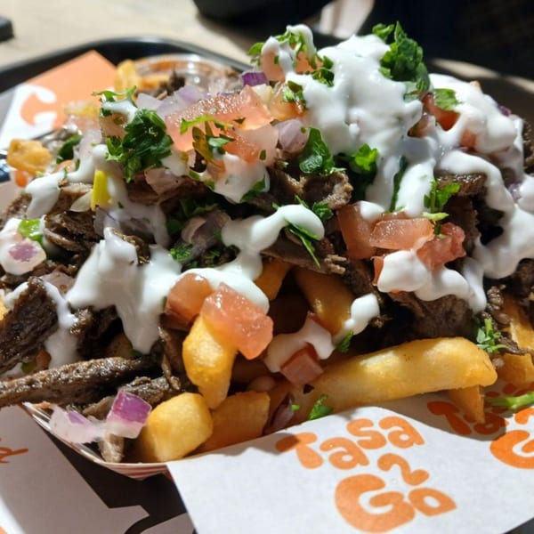 Tasa2Go's Egyptian shawarma fries, topped with meat, white sauce, diced tomatoes, onions, and parsley.